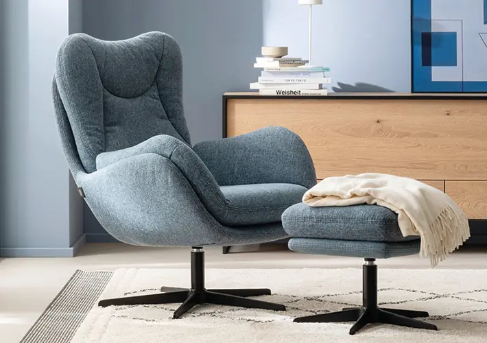 Grauer Relaxsessel mit Hocker vor Sideboard mit Büchern, Lampe und Bild